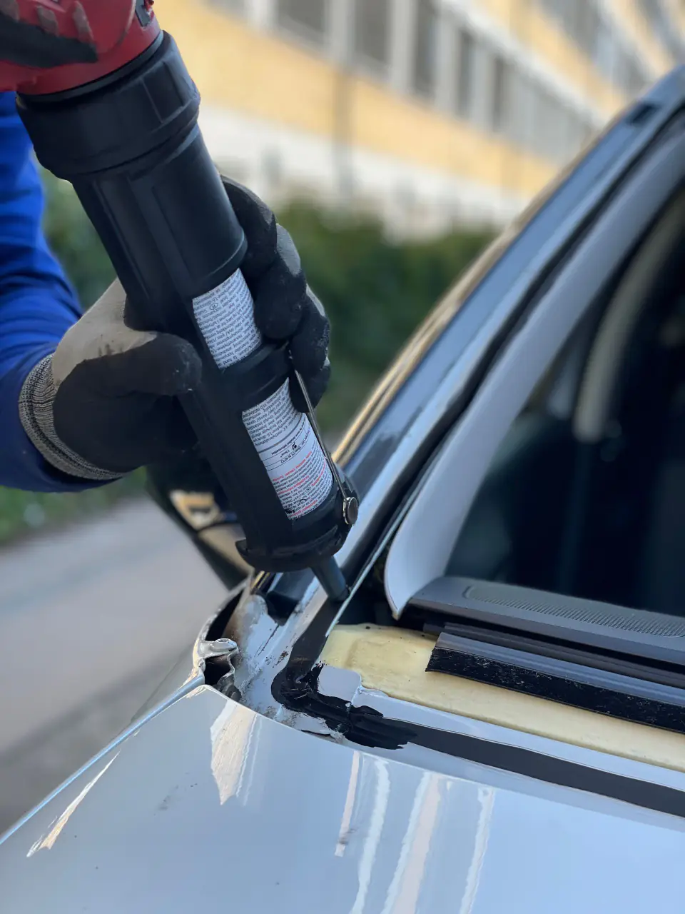 A bead of black urethane adhesive laid along a car's windshield flange before the new glass is set